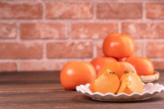 Sliced sweet persimmon kaki in a bamboo sieve basket on dark wooden table with red brick wall background, Chinese lunar new year fruit design concept, close up.