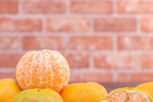 Peeled tangerines in a bamboo sieve basket on dark wooden table with red brick wall background, Chinese lunar new year fruit design concept, close up.