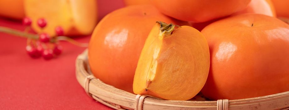 Fresh beautiful sliced sweet persimmon kaki isolated on red table background and bamboo sieve, Chinese lunar new year design concept, close up.