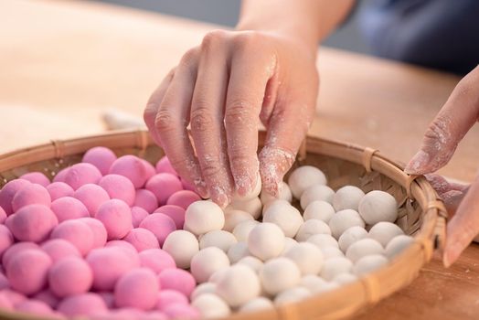 An Asia woman is making Tang yuan, yuan xiao, Chinese traditional food rice dumplings in red and white for lunar new year, winter festival, close up.