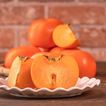 Sliced sweet persimmon kaki in a bamboo sieve basket on dark wooden table with red brick wall background, Chinese lunar new year fruit design concept, close up.