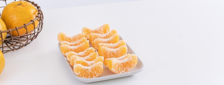 Beautiful peeled tangerines in a plate and metal basket isolated on bright white clean table in a modern contemporary kitchen island, close up.