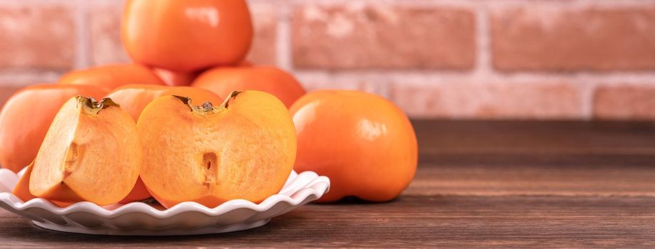 Sliced sweet persimmon kaki in a bamboo sieve basket on dark wooden table with red brick wall background, Chinese lunar new year fruit design concept, close up.