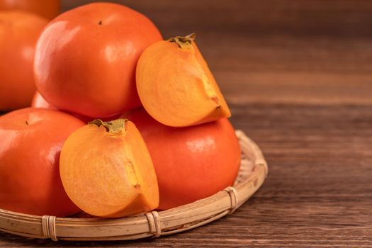 Sliced sweet persimmon kaki in a bamboo sieve basket on dark wooden table with red brick wall background, Chinese lunar new year fruit design concept, close up.