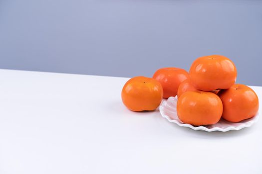 Fresh beautiful sliced sweet persimmon kaki isolated on white kitchen table with gray blue background, Chinese lunar new year design concept, close up.