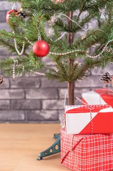 Decorated Christmas tree with wrapped beautiful red and white gifts at home with black brick wall, festive design concept, close up.