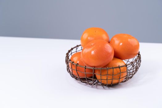 Fresh beautiful sliced sweet persimmon kaki isolated on white kitchen table with gray blue background, Chinese lunar new year design concept, close up.