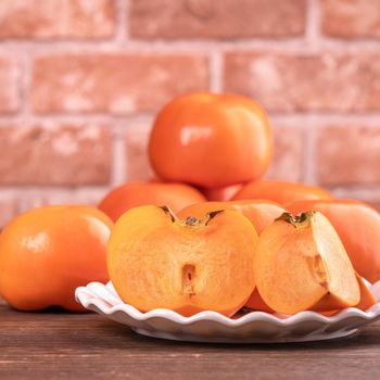 Fresh beautiful sliced sweet persimmon kaki on dark wooden table with red brick wall background, Chinese lunar new year fruit design concept, close up.