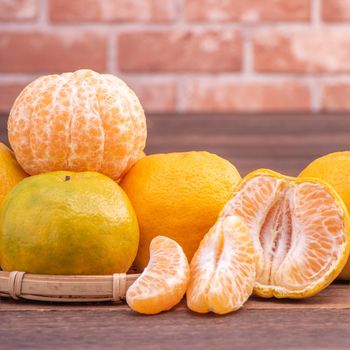 Peeled tangerines in a bamboo sieve basket on dark wooden table with red brick wall background, Chinese lunar new year fruit design concept, close up.