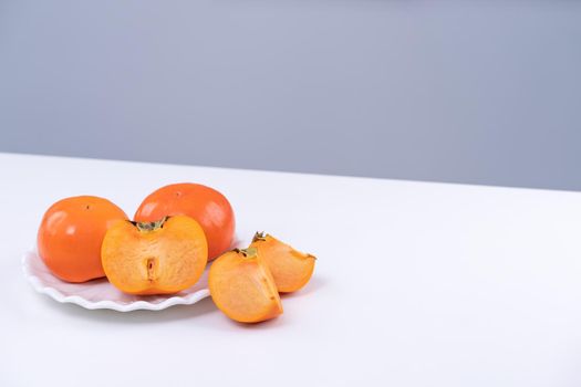 Fresh beautiful sliced sweet persimmon kaki isolated on white kitchen table with gray blue background, Chinese lunar new year design concept, close up.