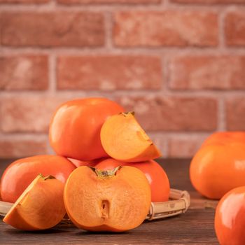 Fresh beautiful sliced sweet persimmon kaki on dark wooden table with red brick wall background, Chinese lunar new year fruit design concept, close up.