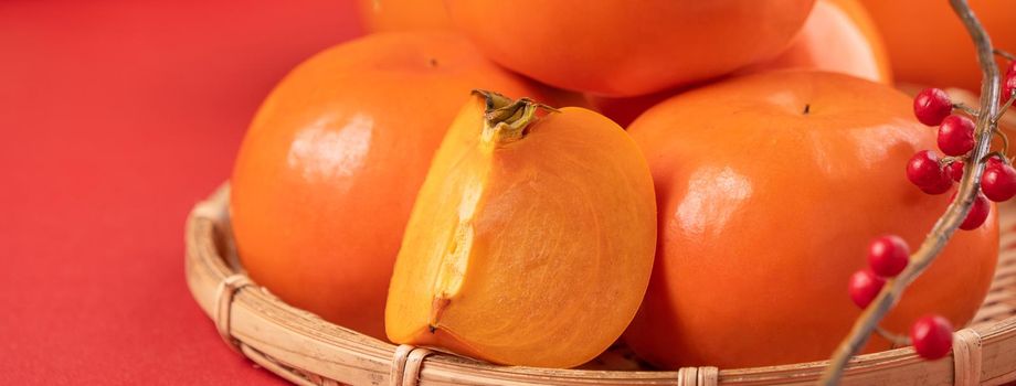 Fresh beautiful sliced sweet persimmon kaki isolated on red table background and bamboo sieve, Chinese lunar new year design concept, close up.