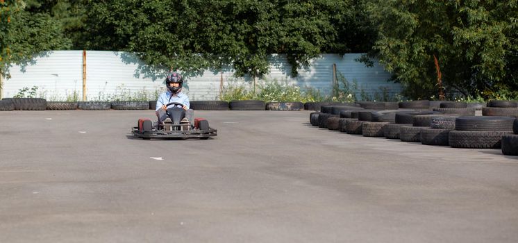 A girl or a woman in a hard hat rides a go-kart on a special track fenced with rubber wheels. Active recreation and sports on transport. Preparation and training for competitions. 