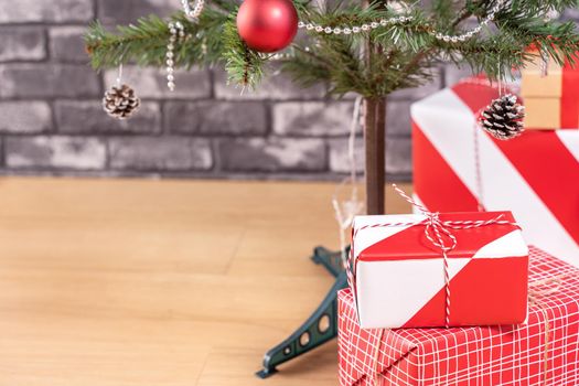 Decorated Christmas tree with wrapped beautiful red and white gifts at home with black brick wall, festive design concept, close up.