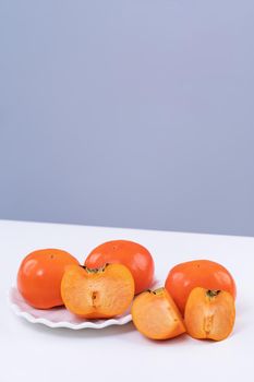 Fresh beautiful sliced sweet persimmon kaki isolated on white kitchen table with gray blue background, Chinese lunar new year design concept, close up.