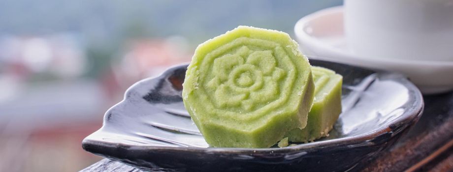 Delicious green mung bean cake with black tea plate on wooden railing of a teahouse in Taiwan with beautiful landscape in background, close up.