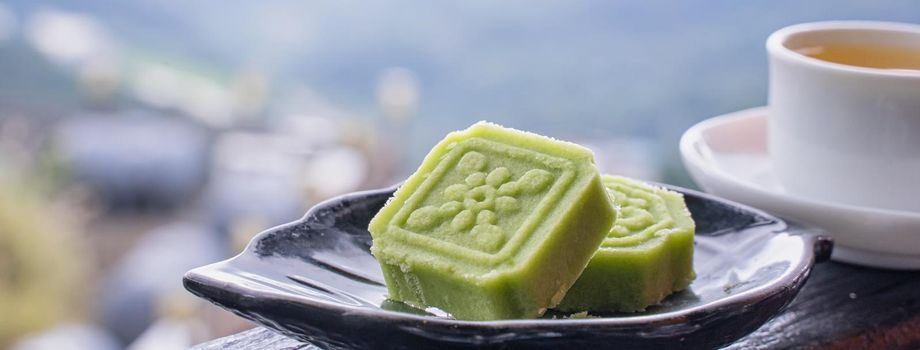 Delicious green mung bean cake with black tea plate on wooden railing of a teahouse in Taiwan with beautiful landscape in background, close up.