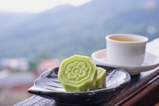 Delicious green mung bean cake with black tea plate on wooden railing of a teahouse in Taiwan with beautiful landscape in background, close up.