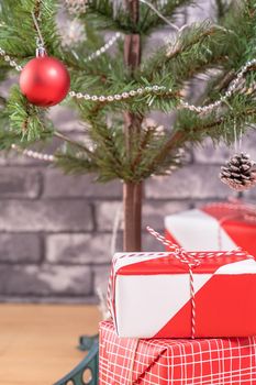 Decorated Christmas tree with wrapped beautiful red and white gifts at home with black brick wall, festive design concept, close up.