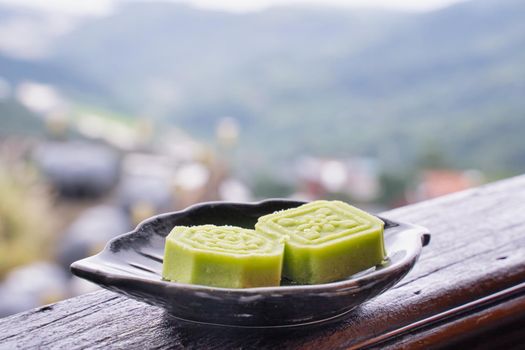 Delicious green mung bean cake with black tea plate on wooden railing of a teahouse in Taiwan with beautiful landscape in background, close up.