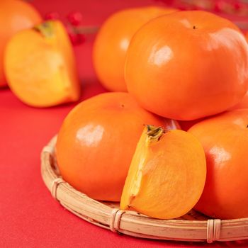 Fresh beautiful sliced sweet persimmon kaki isolated on red table background and bamboo sieve, Chinese lunar new year design concept, close up.