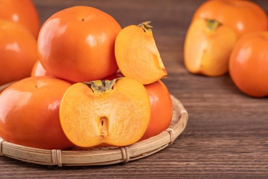 Fresh, beautiful orange color persimmon kaki on bamboo sieve over dark wooden table. Seasonal, traditional fruit of Chinese lunar new year, close up.