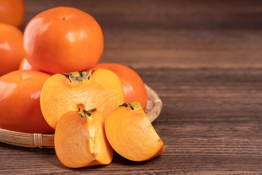 Fresh, beautiful orange color persimmon kaki on bamboo sieve over dark wooden table. Seasonal, traditional fruit of Chinese lunar new year, close up.