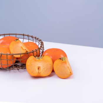 Fresh beautiful sliced sweet persimmon kaki isolated on white kitchen table with gray blue background, Chinese lunar new year design concept, close up.