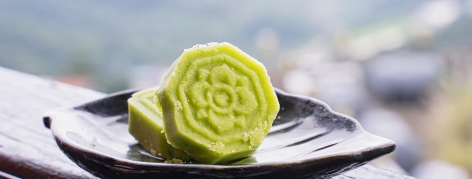 Delicious green mung bean cake with black tea plate on wooden railing of a teahouse in Taiwan with beautiful landscape in background, close up.