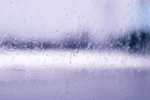 Raindrops on glass close up, blurred purple background