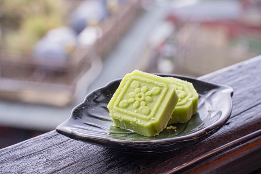 Delicious green mung bean cake with black tea plate on wooden railing of a teahouse in Taiwan with beautiful landscape in background, close up.