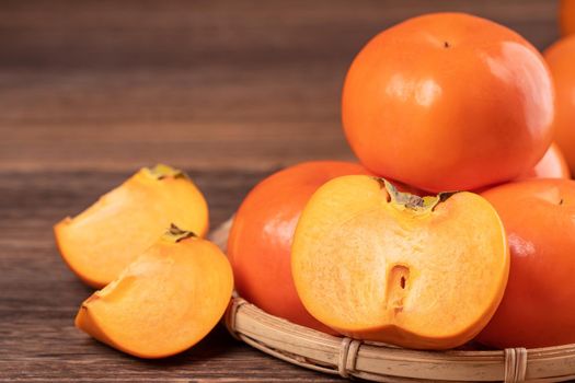 Fresh, beautiful orange color persimmon kaki on bamboo sieve over dark wooden table. Seasonal, traditional fruit of Chinese lunar new year, close up.