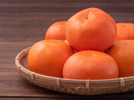 Fresh, beautiful orange color persimmon kaki on bamboo sieve over dark wooden table. Seasonal, traditional fruit of Chinese lunar new year, close up.