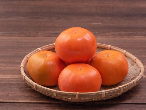 Fresh, beautiful orange color persimmon kaki on bamboo sieve over dark wooden table. Seasonal, traditional fruit of Chinese lunar new year, close up.