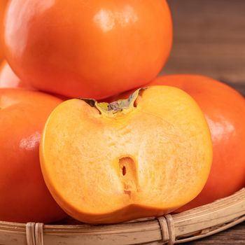 Fresh, beautiful orange color persimmon kaki on bamboo sieve over dark wooden table. Seasonal, traditional fruit of Chinese lunar new year, close up.