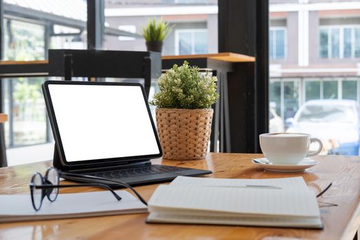 Shot of digital tablet with blank white screen, keyboard, cup of coffee on workspace desk.