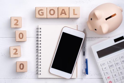 2020 goal, finance plan abstract design concept, wood blocks on white table background with piggy bank, cell phone, top view, flat lay, copy space.