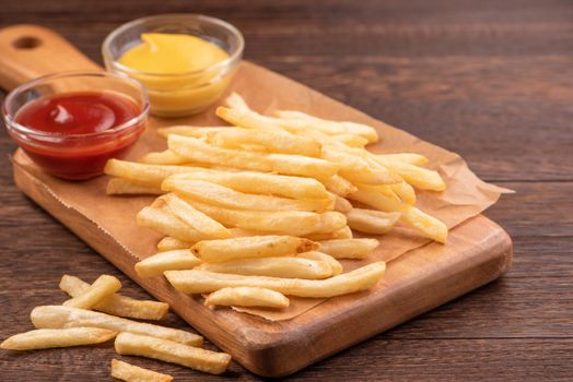 Golden yummy deep French fries on kraft baking sheet paper and serving tray to eat with ketchup and yellow mustard, close up, lifestyle.