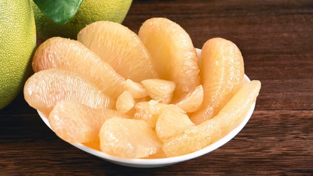 Fresh peeled pomelo, grapefruit, shaddock with green leaves on dark wooden plank table. Seasonal fruit near mid-autumn festival, close up, copy space