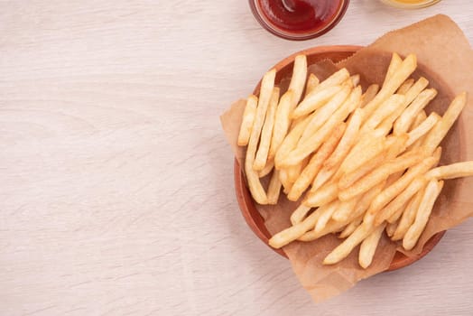 Golden yummy deep French fries on kraft baking sheet paper and serving tray to eat with ketchup and yellow mustard, top view, lifestyle.