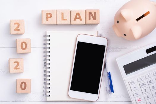 2020 goal, finance plan abstract design concept, wood blocks on white table background with piggy bank, cell phone, top view, flat lay, copy space.