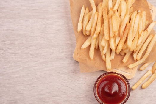 Golden yummy deep French fries on kraft baking sheet paper and serving tray to eat with ketchup and yellow mustard, top view, lifestyle.