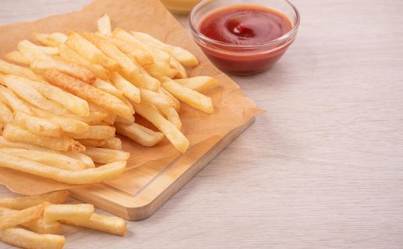 Golden yummy deep French fries on kraft baking sheet paper and serving tray to eat with ketchup and yellow mustard, top view, lifestyle.