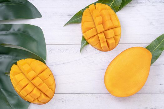 Beautiful chopped ripe mango with green leaves on bright white color wooden background, top view, flat lay, copy space. Tropical fruit design concept.
