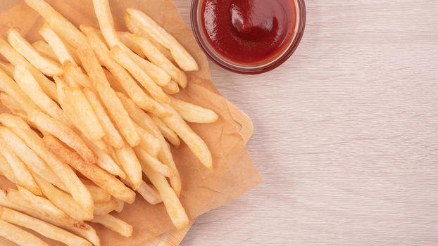 Golden yummy deep French fries on kraft baking sheet paper and serving tray to eat with ketchup and yellow mustard, top view, lifestyle.