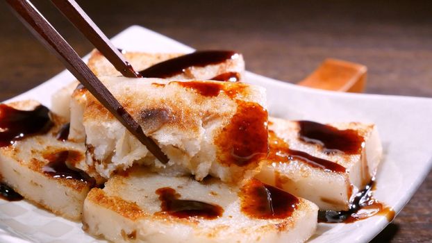Pouring black soy sauce on ready-to-eat delicious turnip cake, Chinese traditional local dish radish cake in restaurant, close up, copy space.