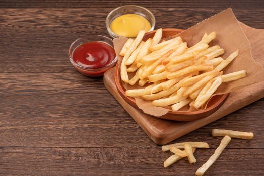 Golden yummy deep French fries on kraft baking sheet paper and serving tray to eat with ketchup and yellow mustard, top view, lifestyle.