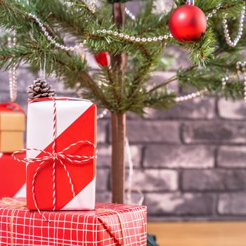 Decorated Christmas tree with wrapped beautiful red and white gifts at home with black brick wall, festive design concept, close up.