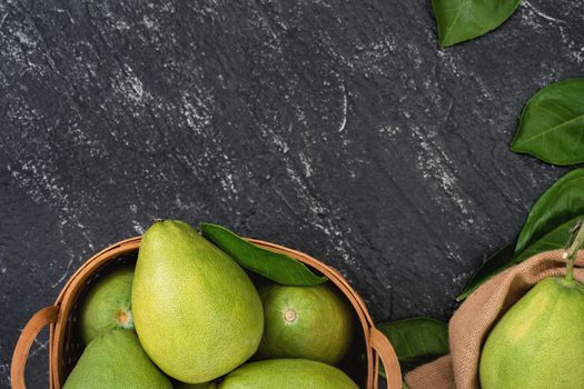 Fresh peeled pomelo, pummelo, grapefruit, shaddock on dark background in bamboo basket. Autumn seasonal fruit, top view, flat lay, tabletop shot.