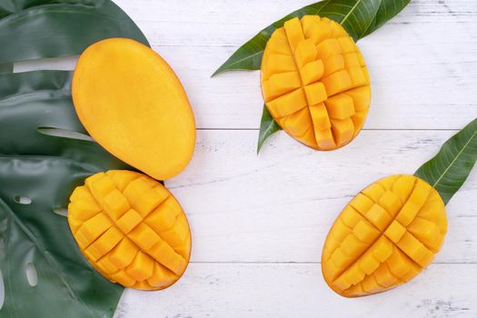 Beautiful chopped ripe mango with green leaves on bright white color wooden background, top view, flat lay, copy space. Tropical fruit design concept.
